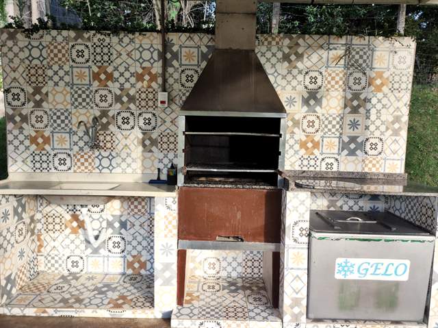 Churrasqueira de alvenaria com bancada de azulejo e fogão ao lado