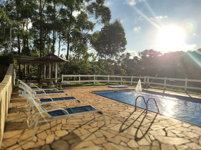 Piscina com espreguiçadeiras ao sol e cerca branca em volta